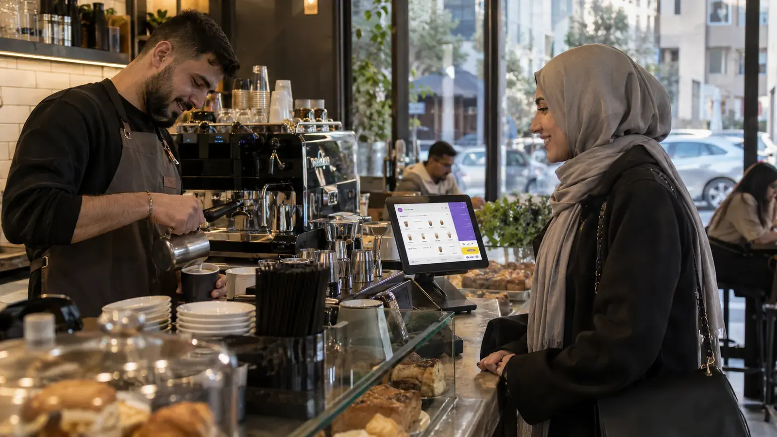موظف في مقهى يجهّز طلب زبونة، وبجانبه شاشة الطلبات